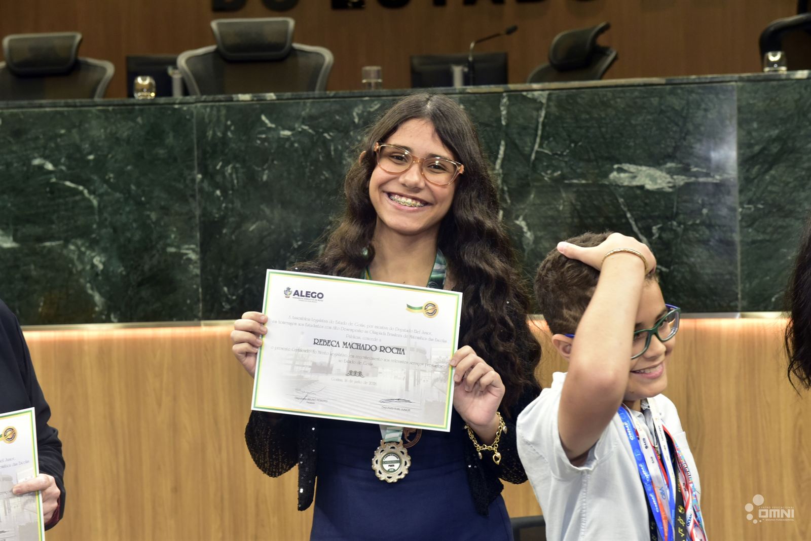 Aluna do OMNI comemorando com certificado e medalha da Olimpíada de Matemática na Alego